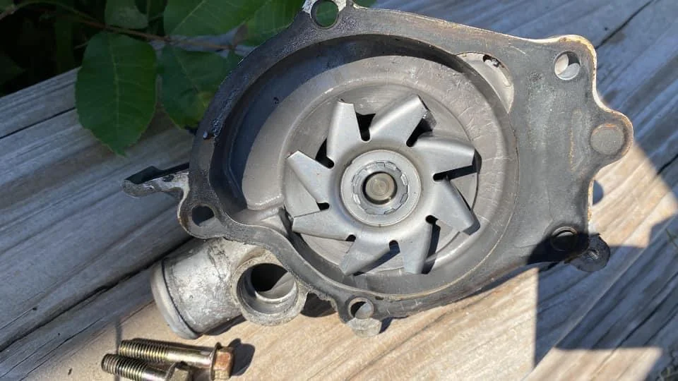 A close photo of the front of an engine showing dried coolant residue and wetness near the water pump area and pulley