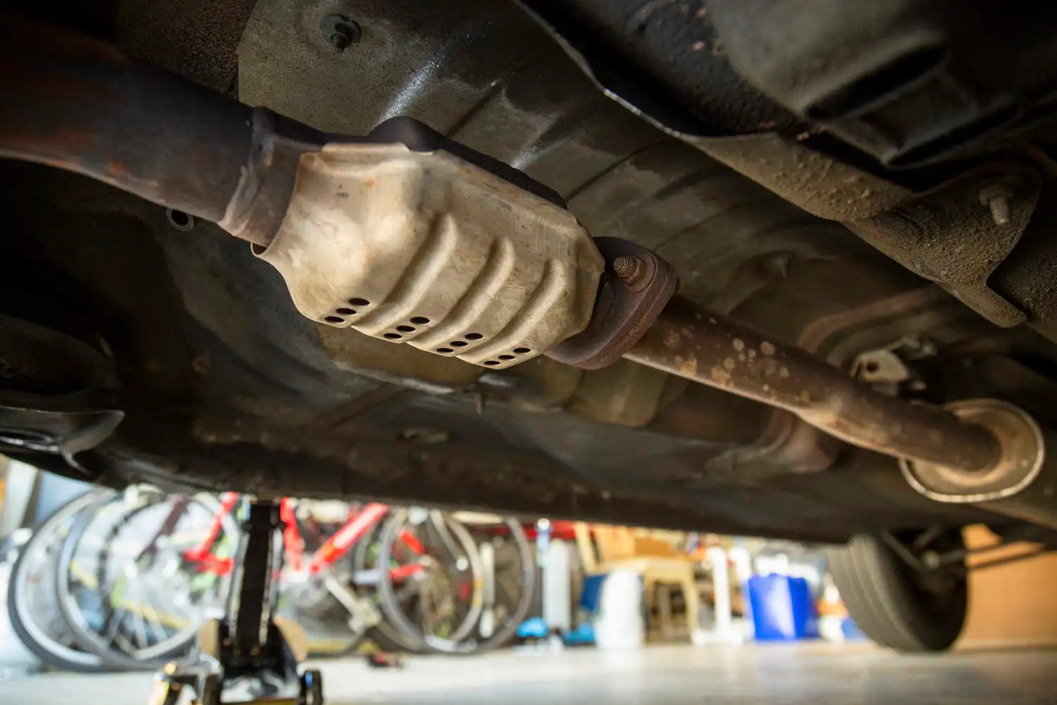 A close-up photo of a catalytic converter installed in the exhaust system under a vehicle, showing heat shielding and adjacent exhaust piping