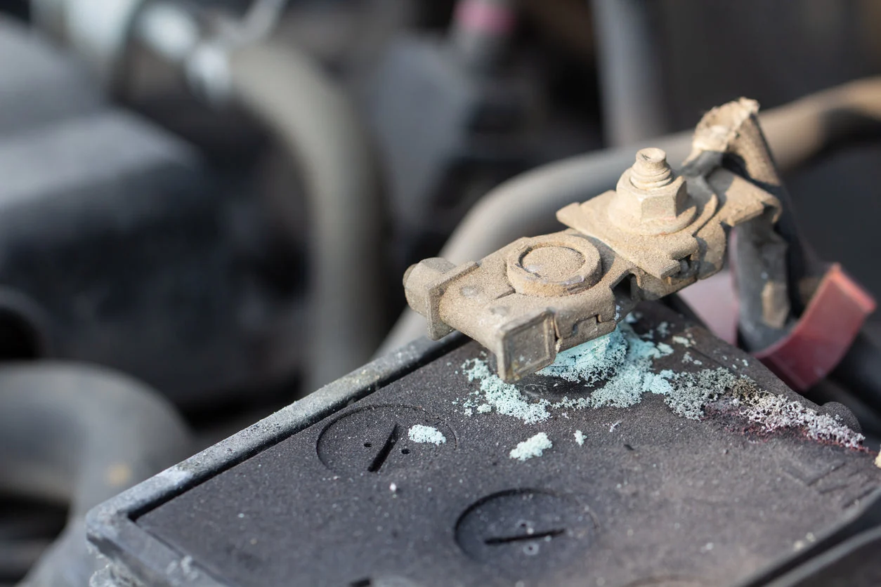 A close-up view of a car battery terminal with visible white and blue corrosion buildup around the connector