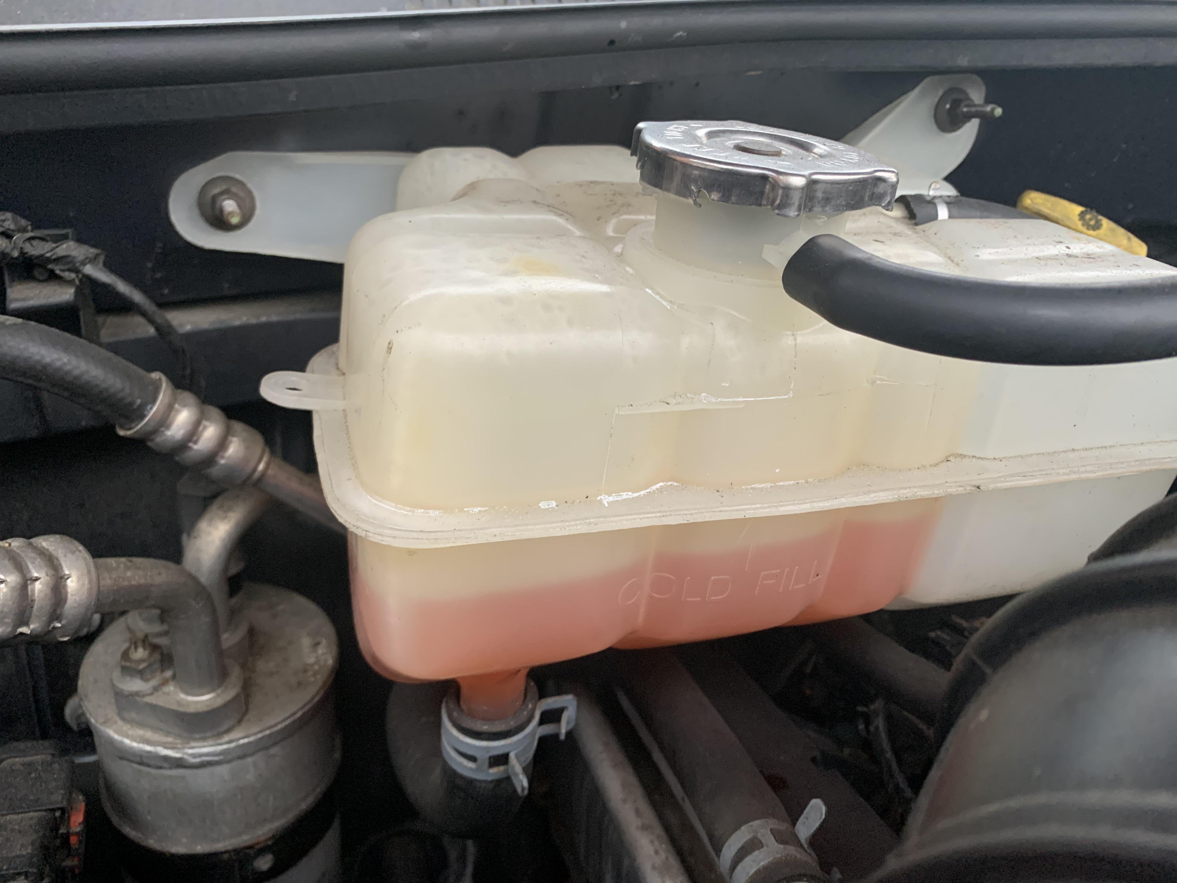 A close view of a car coolant overflow reservoir with the fluid level visibly below the MIN line, photographed under an open hood