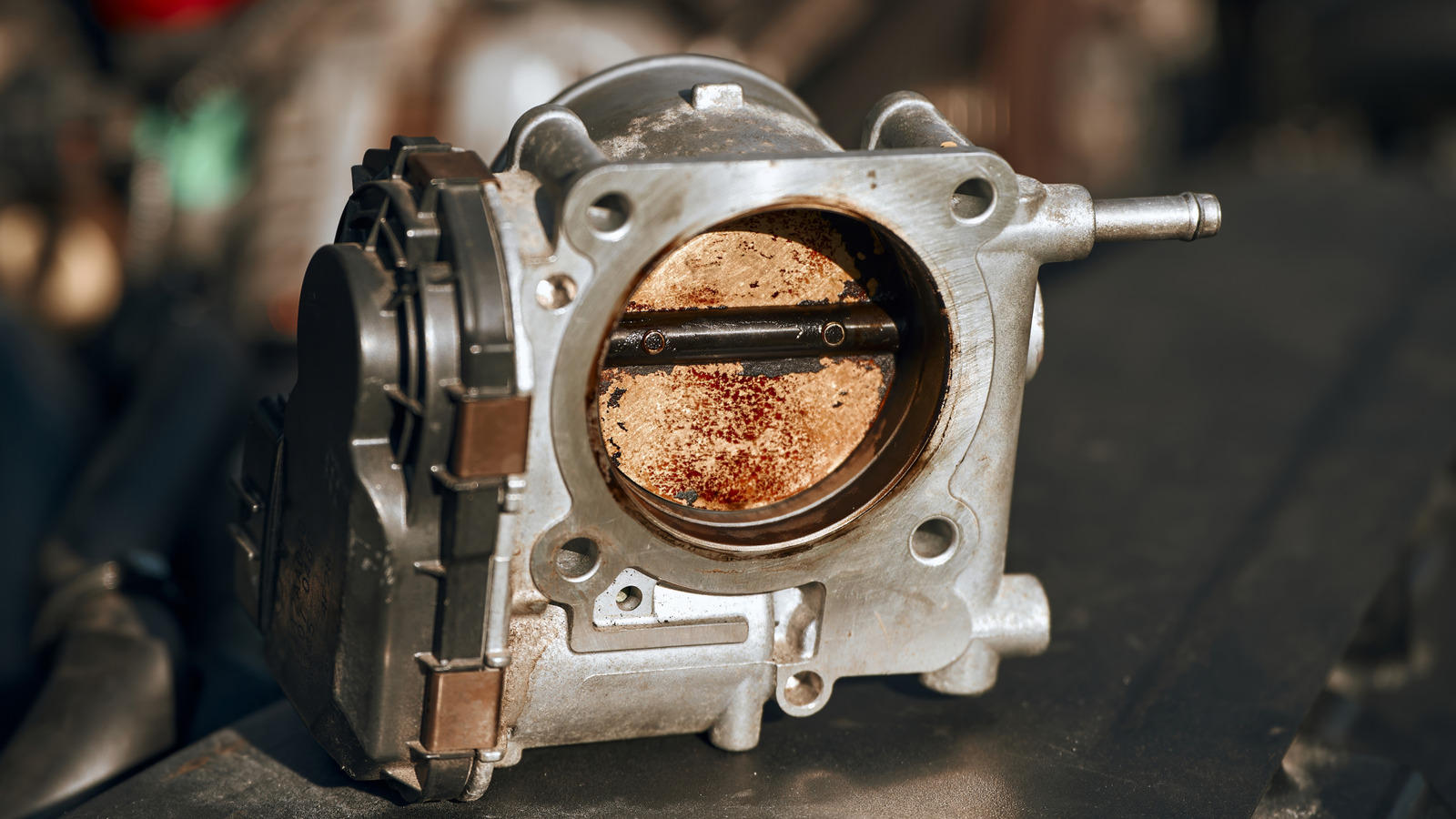 A close view of a car throttle body with visible carbon deposits around the throttle plate