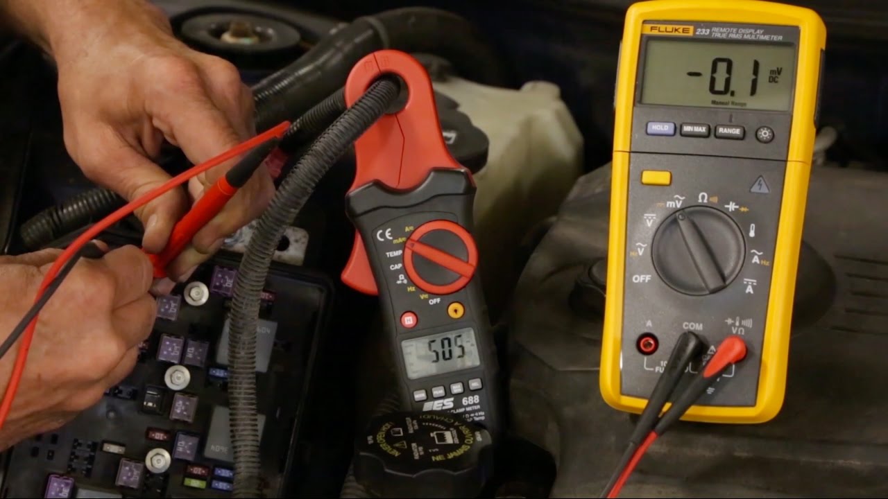A digital multimeter connected in series at a car battery negative terminal while measuring parasitic current draw in an engine bay