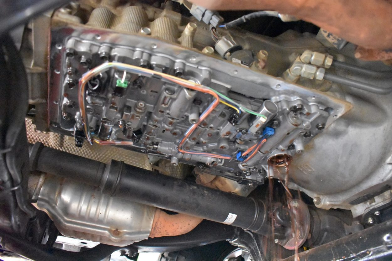 A mechanic draining automatic transmission fluid into a clean catch pan under a vehicle on a lift