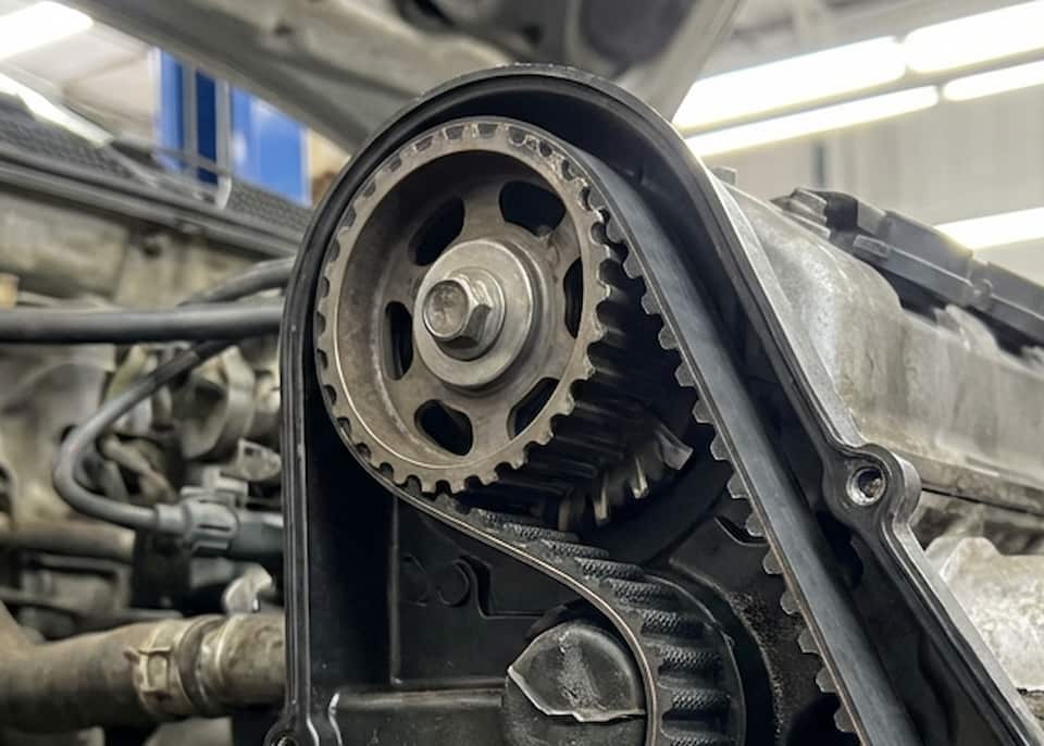 A mechanic working on a timing belt area with the front engine covers removed, hands holding a ratchet near the crank pulley