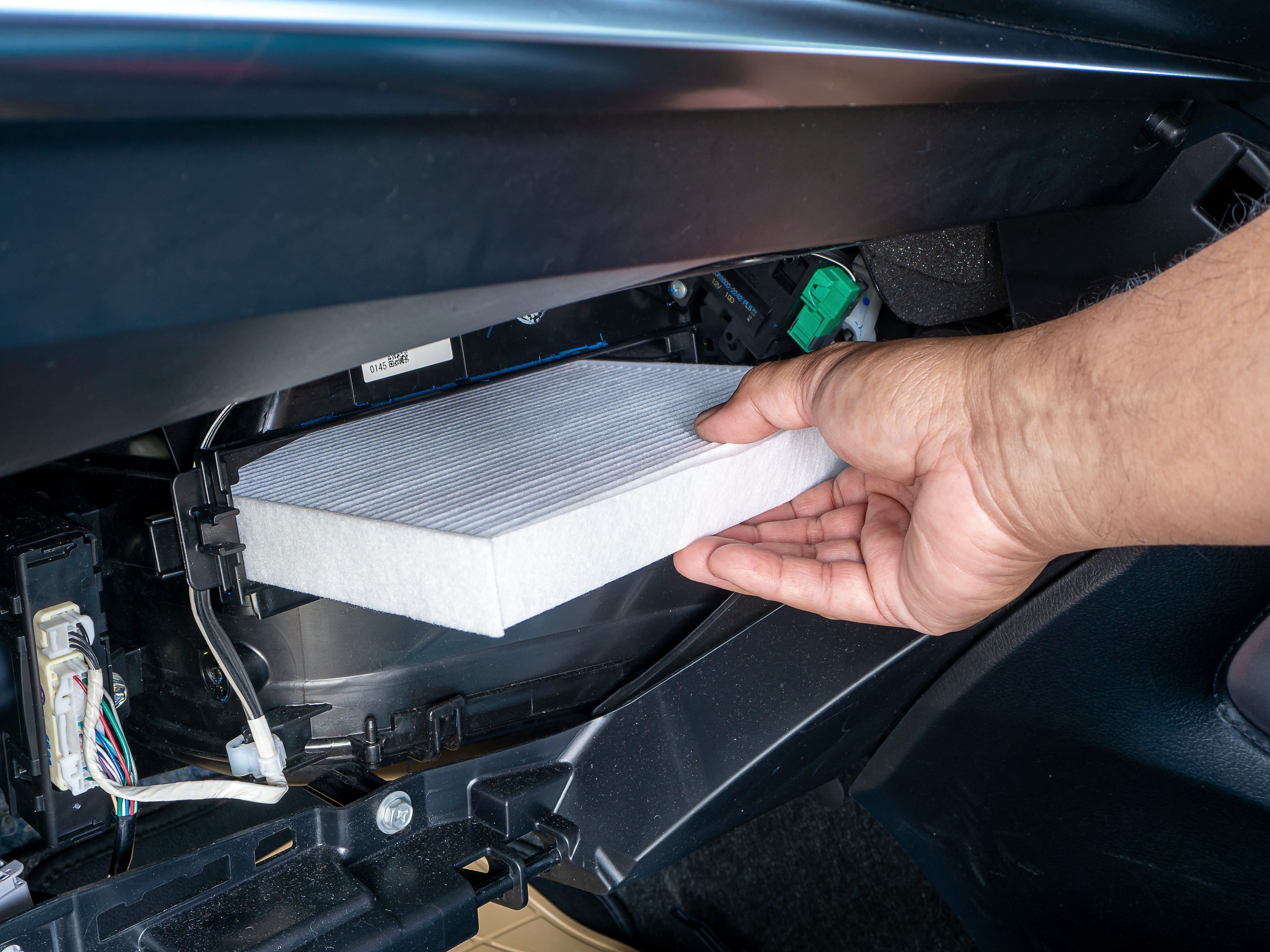 A person holding a dirty cabin air filter next to a new clean filter beside an open glove box in a car