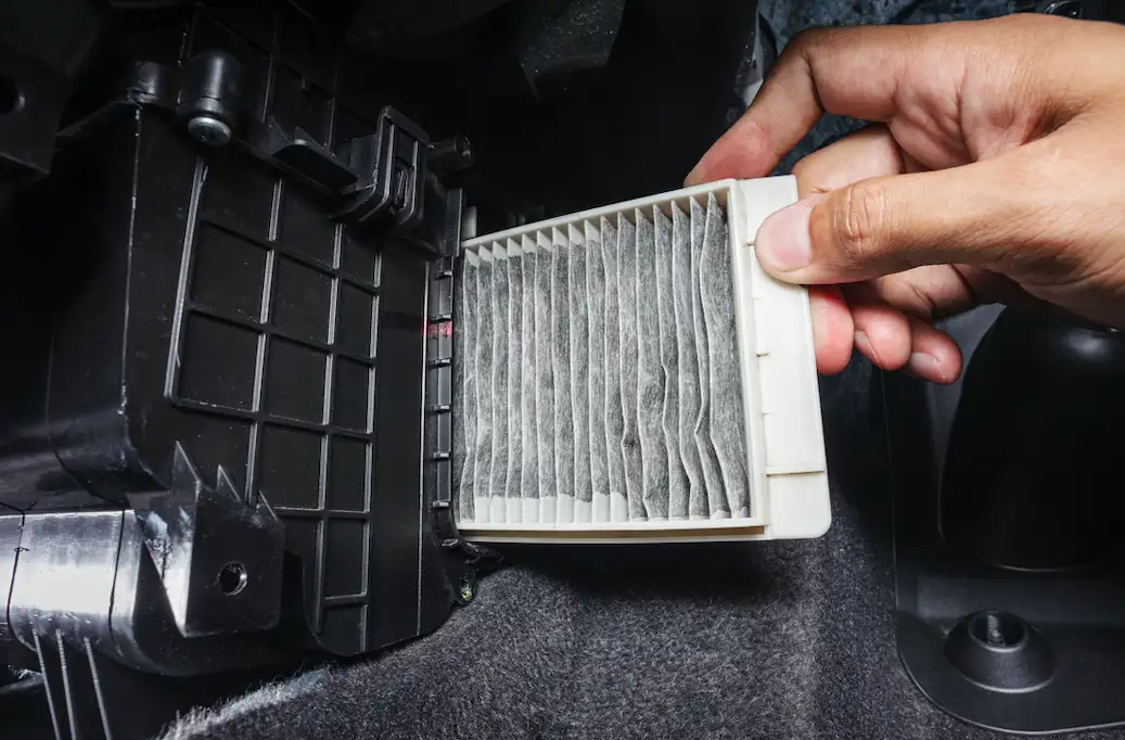 A photo of a gloved hand holding a heavily dust-covered cabin air filter removed from behind a car glovebox