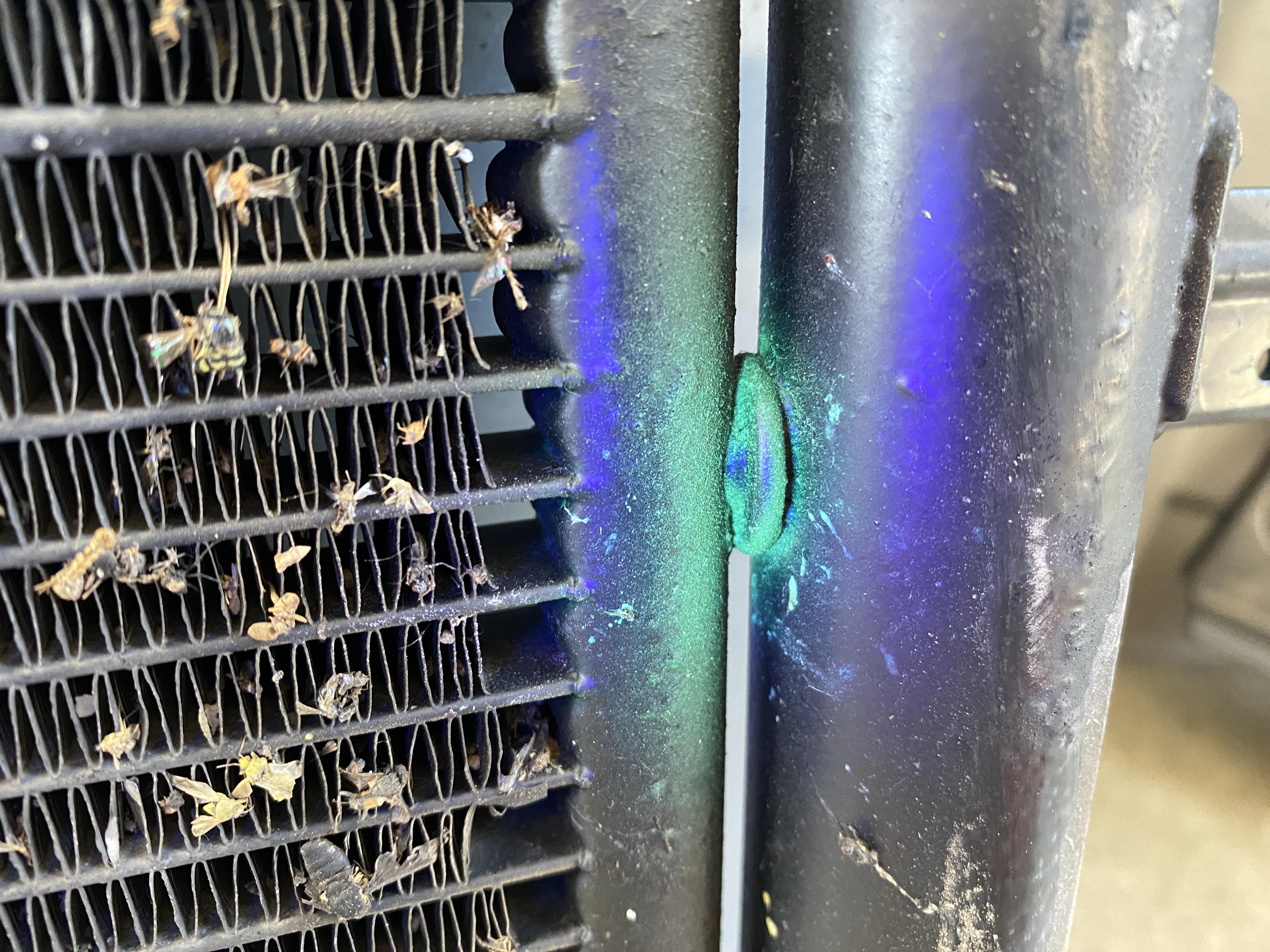 A photo of the front of a vehicle with the grille removed, showing the air conditioning condenser fins and visible oily grime near one corner