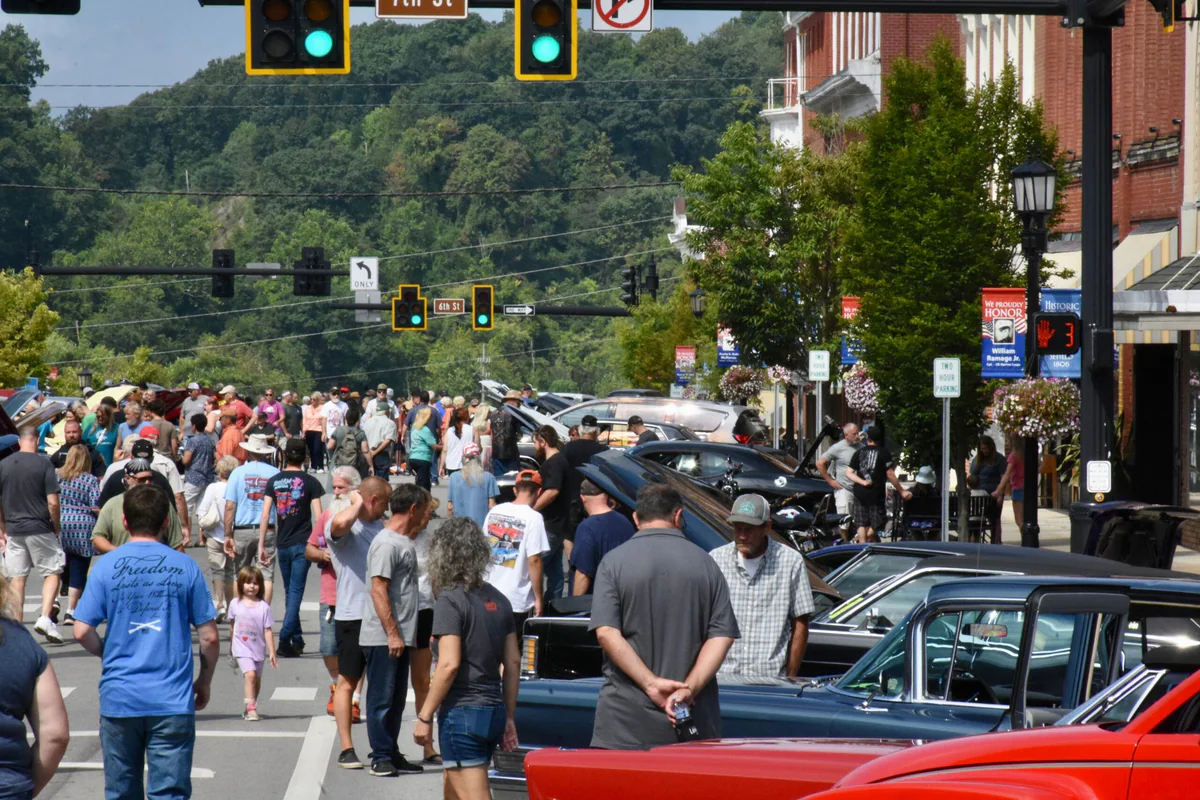 A row of modern muscle cars parked diagonally along a curb near Marietta Square with owners standing nearby talking
