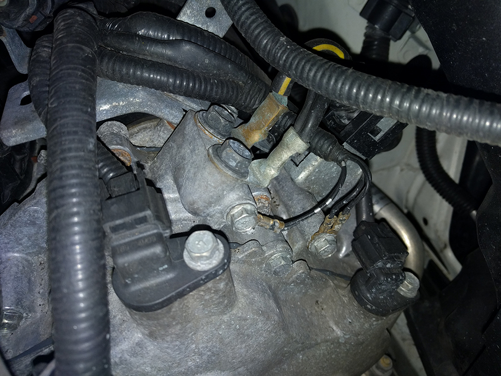 Black jumper cable clamp attached to a clean, unpainted metal bracket on the engine block away from the battery