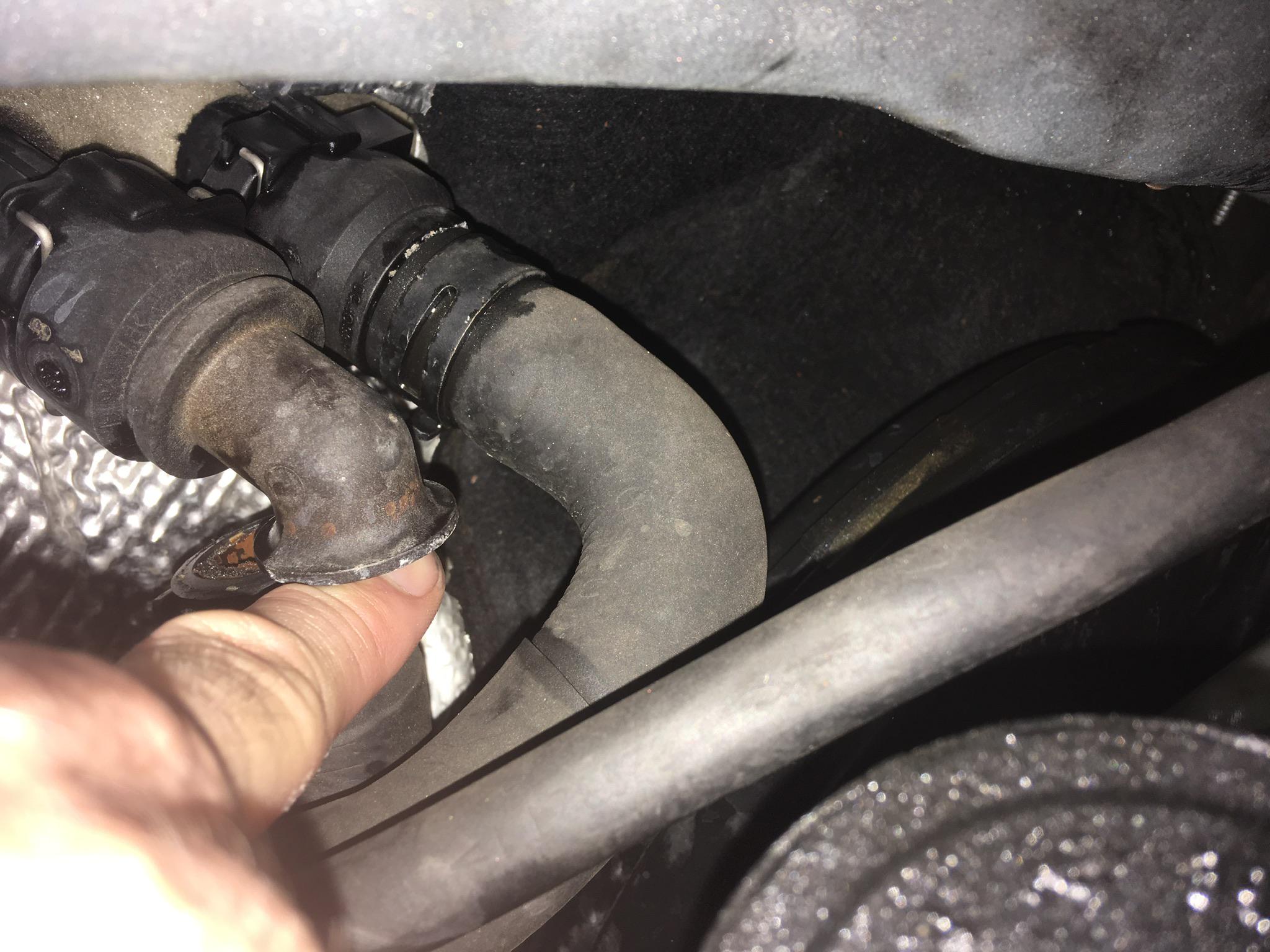 Two heater hoses entering the firewall with a gloved hand pointing at the connections